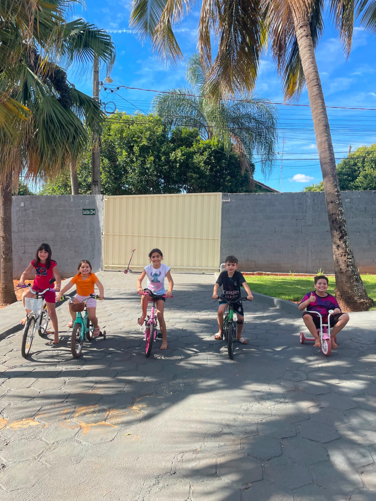 Crianças andando de bicicleta e triciclo na área externa arborizada da Talsce.