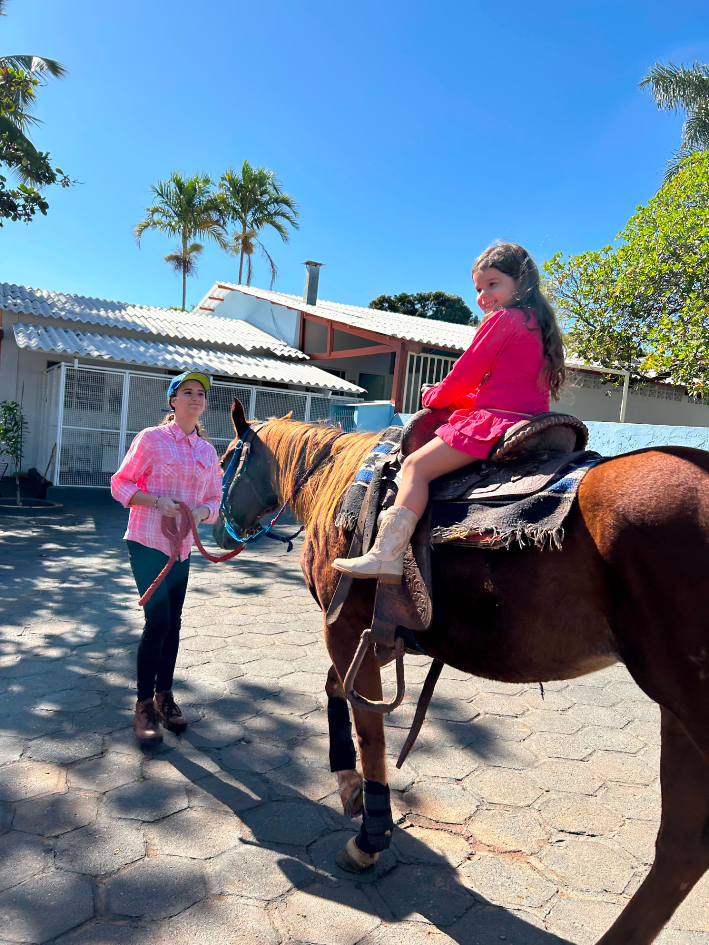 Criança montada em um cavalo acompanhada por uma instrutora em atividade externa.